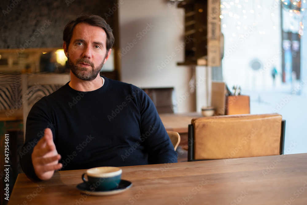 Middle aged caucasian male sitting at the table in coffee shop explaining stuff Middle aged caucasian male sitting at the table in coffee shop explaining stuff