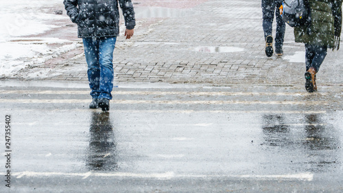 Winter City Slippery Sidewalk. Feet of people walking along the icy snowy pavement in crosswalk in snowfall. Pair of shoe on icy road in winter. Abstract empty blank winter weather background.