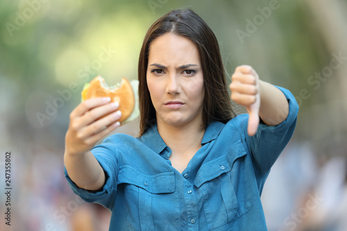 Annoyed woman holding a burger with thumb down