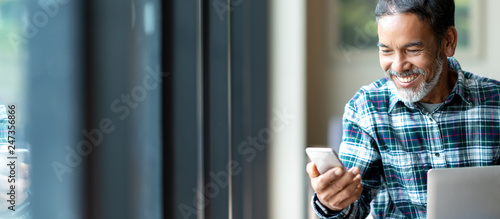 Banner of happy mature asian or hispanic old man looking at smartphone smiling positive in casual lifestyle with digital technology of older or senior guy concept. Urban elderly asian retired man.
