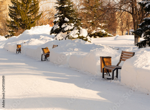Fototapeta Naklejka Na Ścianę i Meble -  Snow-covered wooden bench in the city park in the morning.