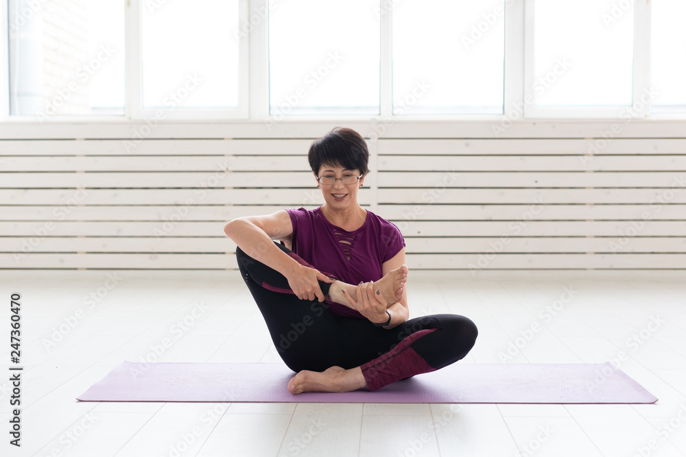 People, yoga, sport and healthcare concept - Attractive middle-aged woman stretching and sitting in yoga lotus position