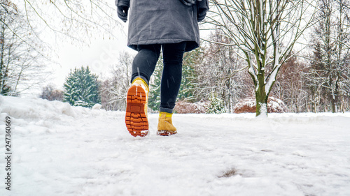 Winter Walk in Yellow Leather Boots. Back view on the feet of a women walking along the icy snowy pavement. Pair of shoe on icy road in winter. Abstract empty blank winter weather background