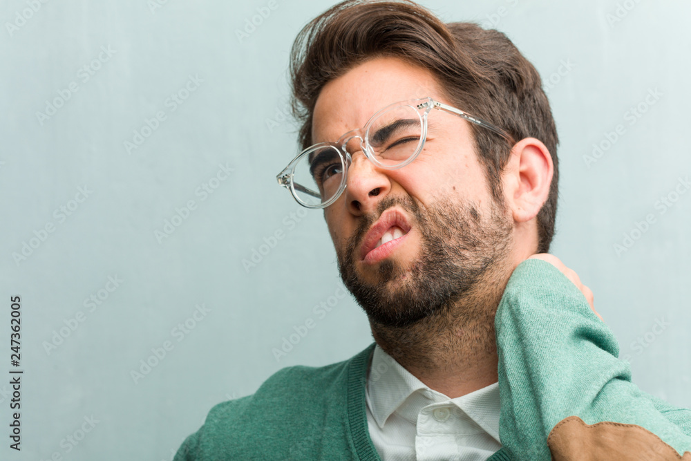 Fototapeta premium Young handsome entrepreneur man face closeup with back pain due to work stress, tired and astute