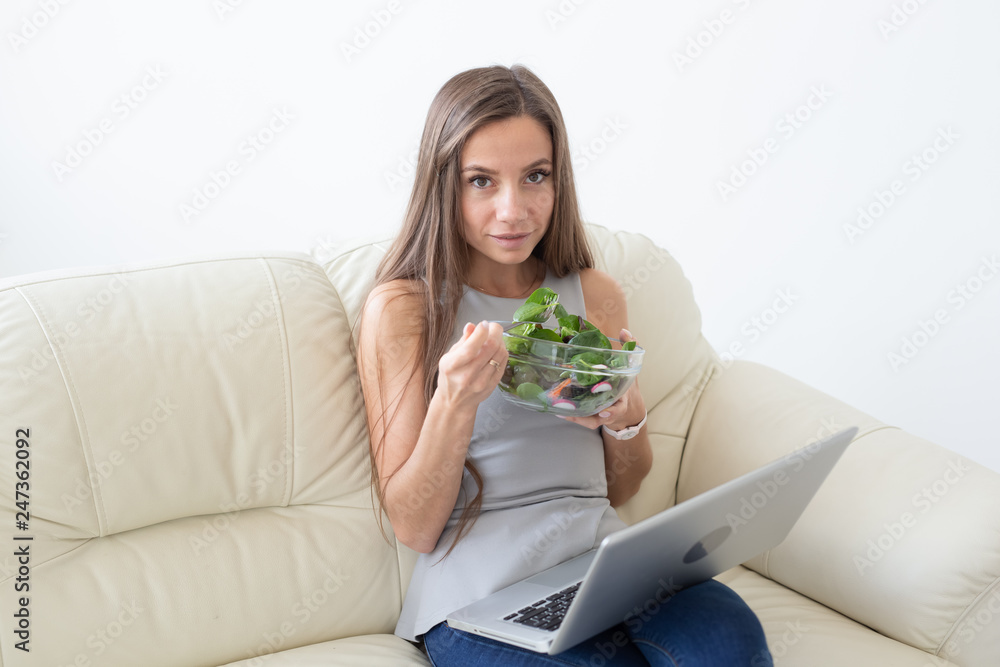 Healthy lifestyle, proper diet, relax and people concept- young beautiful woman sitting on the white sofa and eating a salad