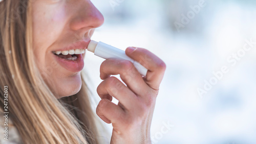 Happy woman applying lip balm in winter holiday in a snowy mountain