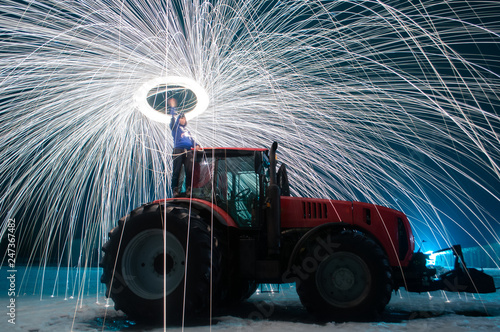 Man sparks on the background of a red tractor, steel wool photo, sparks on a long exposure,