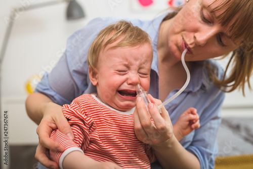 toddler boy crying while his mother trying to clean his nose