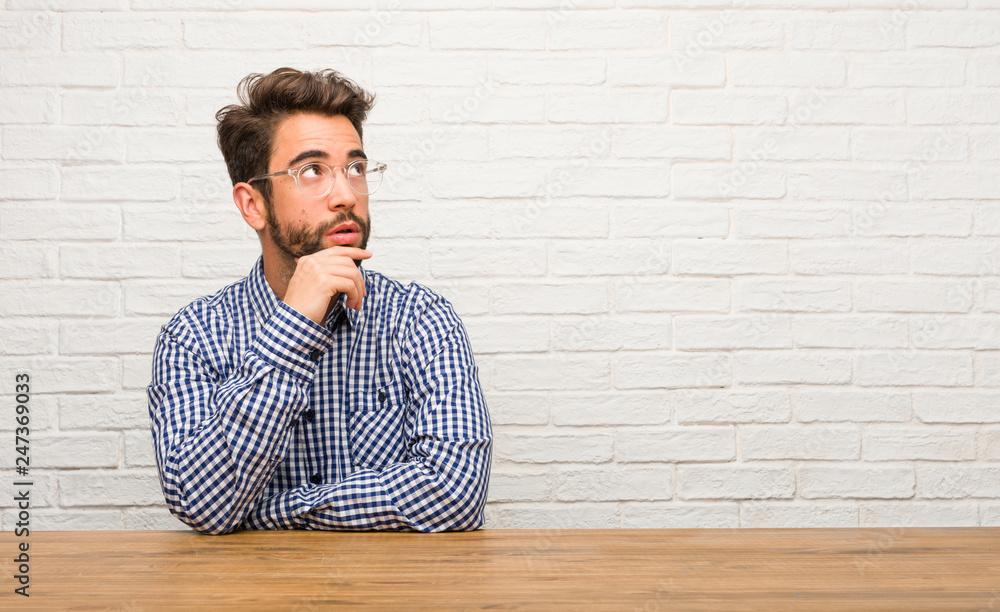 Young caucasian man sitting thinking and looking up, confused about an idea, would be trying to find a solution Young caucasian man sitting thinking and looking up, confused about an idea, would be trying to find a solution