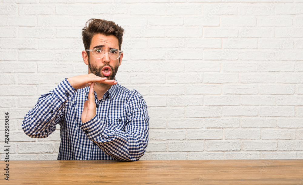 Young caucasian man sitting tired and bored, making a timeout gesture, needs to stop because of work stress, time concept Young caucasian man sitting tired and bored, making a timeout gesture, needs to stop because of work stress, time concept