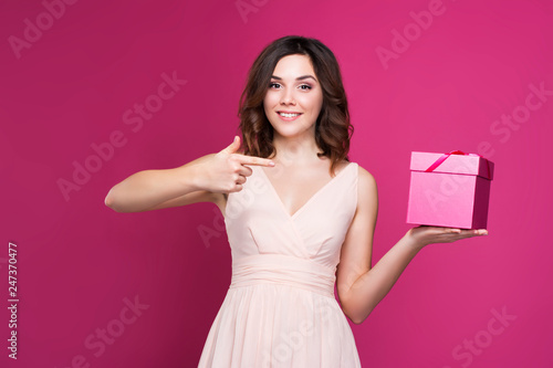 smiling brunette in a dress holding a gift box in her hands