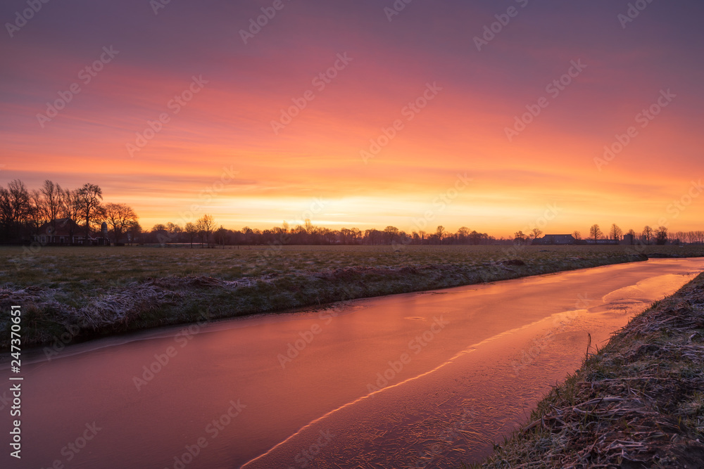 Colourful, winter sunrise over a small canal in the Dutch countryside. Groningen province, Holland.