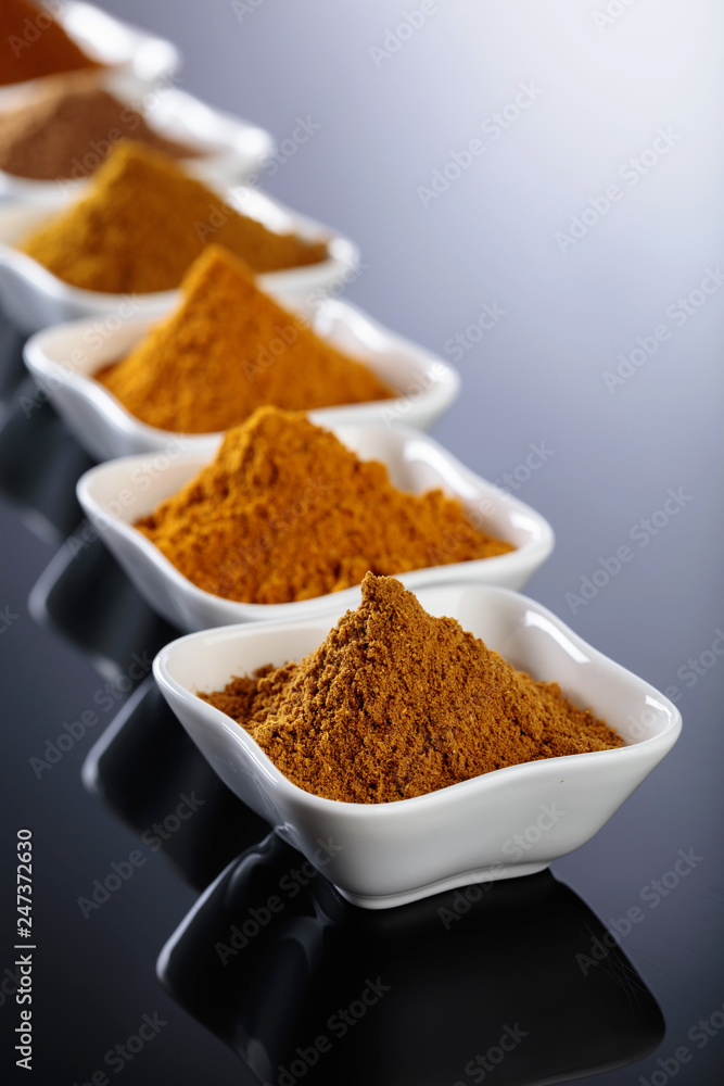 Small white ceramic bowls of Indian spices on black reflective background. Small white ceramic bowls of Indian spices on black reflective background.
