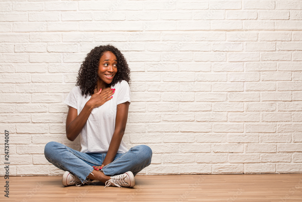 Young black woman sitting on a wooden floor doing a romantic gesture, in love with someone or showing affection for some friend Young black woman sitting on a wooden floor doing a romantic gesture, in love with someone or showing affection for some friend