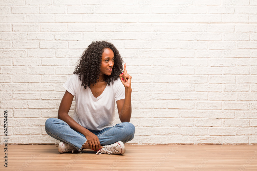 Young black woman sitting on a wooden floor showing number one, symbol of counting, concept of mathematics, confident and cheerful Young black woman sitting on a wooden floor showing number one, symbol of counting, concept of mathematics, confident and cheerful