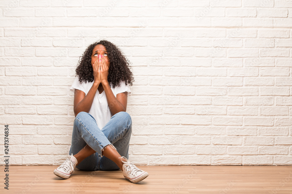 Young black woman sitting on a wooden floor very scared and afraid, desperate for something, cries of suffering and open eyes, concept of madness Young black woman sitting on a wooden floor very scared and afraid, desperate for something, cries of suffering and open eyes, concept of madness