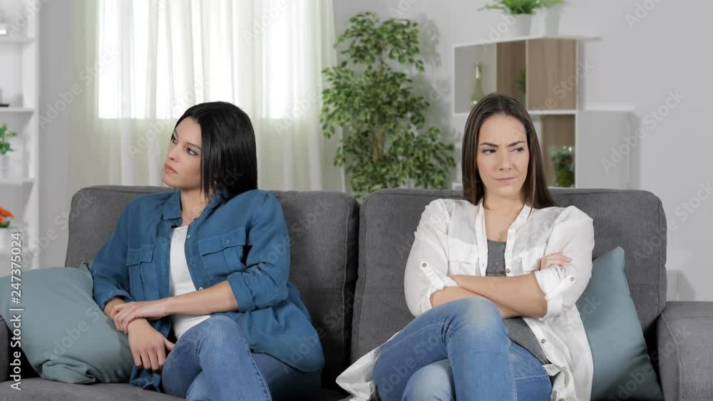 Two angry friends at home ignoring each other sitting on a couch looking at side Two angry friends at home ignoring each other sitting on a couch looking at side