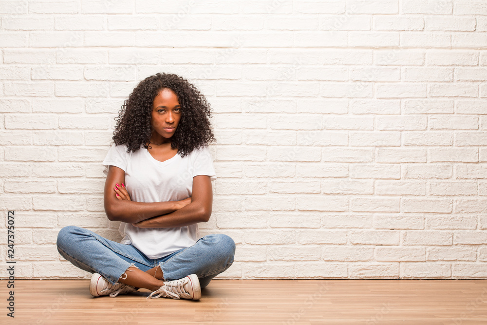 Young black woman sitting on wooden floor very angry and upset, very tense, screaming furious, negative and crazy Young black woman sitting on wooden floor very angry and upset, very tense, screaming furious, negative and crazy