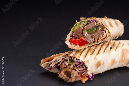 Foto Shawarma sandwich - fresh roll of thin lavash or pita bread filled with grilled meat, mushrooms, cheese, cabbage, carrots, sauce, green