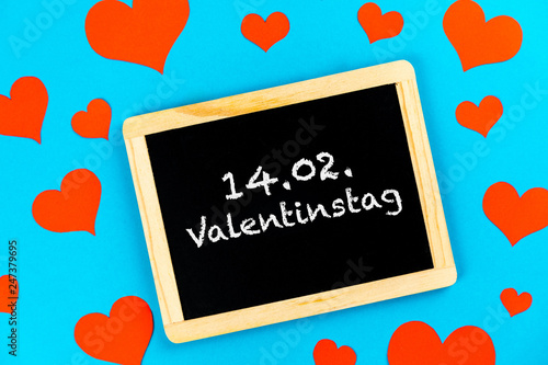chalkboard with red hearts on a blue background with german text 14.02. Valentinstag, in english 14.02. valentines day