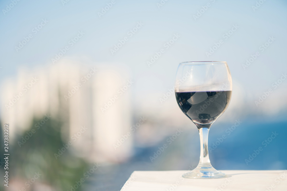 Close up of glass of red wine against the background of blurred town with bokeh at summer evening