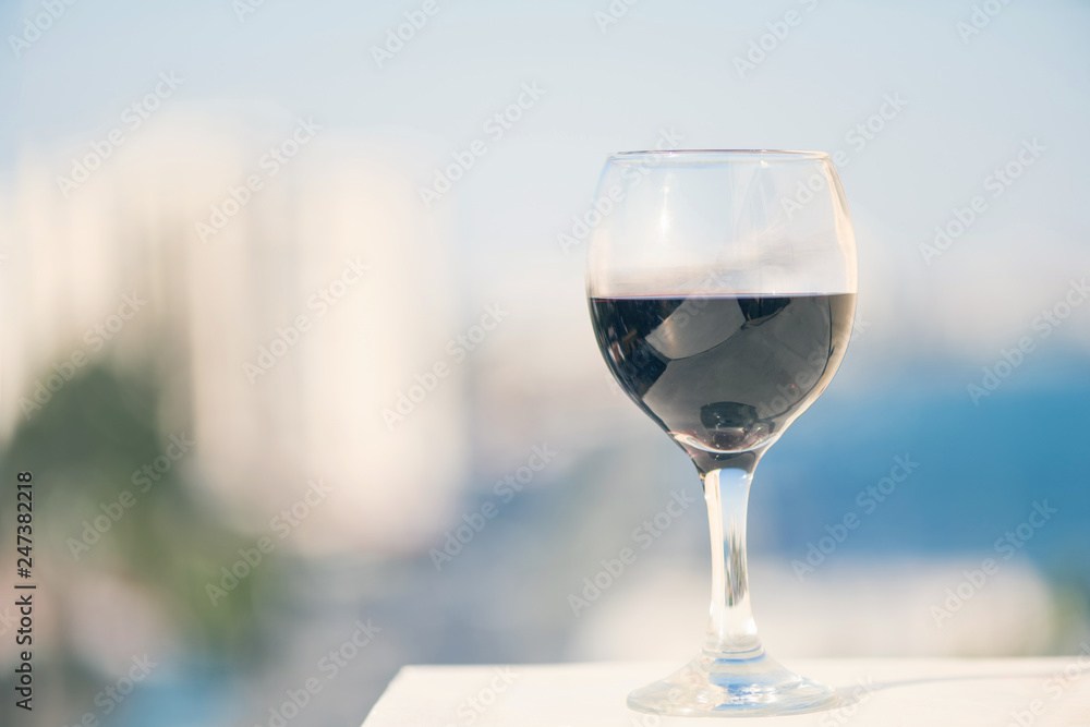 Obraz premium Close up of glass of red wine against the background of blurred town with bokeh at summer evening