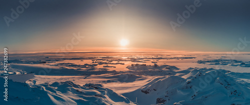 Bright sunset panorama view in Antarctica. Orange sun lights over the snow covered polar surface. Picturesque winter landscape. The beauty of the wild untouched Antarctic nature.