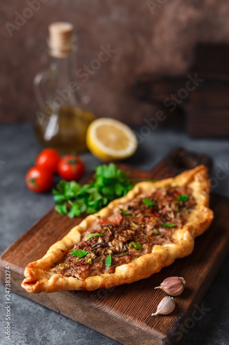 Turkish handmade pide lies on an blue surface. Cherry tomatoes, parsley, lemon, hot pepper, garlic are on the table.