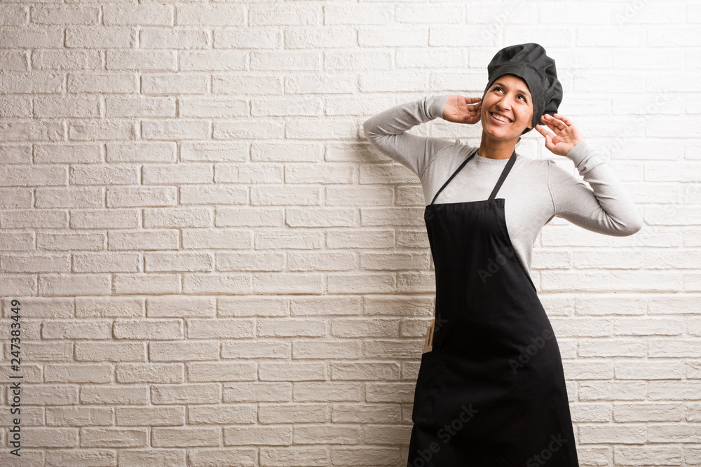 Young baker indian woman against a bricks wall Listening to music, dancing and having fun, moving, shouting and expressing happiness, freedom concept Young baker indian woman against a bricks wall Listening to music, dancing and having fun, moving, shouting and expressing happiness, freedom concept