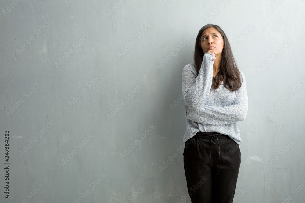 Young indian woman against a grunge wall doubting and confused, thinking of an idea or worried about something Young indian woman against a grunge wall doubting and confused, thinking of an idea or worried about something