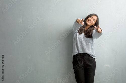 Young indian woman against a grunge wall cheerful and smiling pointing to the front