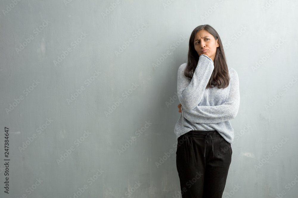 Young indian woman against a grunge wall thinking and looking up, confused about an idea, would be trying to find a solution Young indian woman against a grunge wall thinking and looking up, confused about an idea, would be trying to find a solution