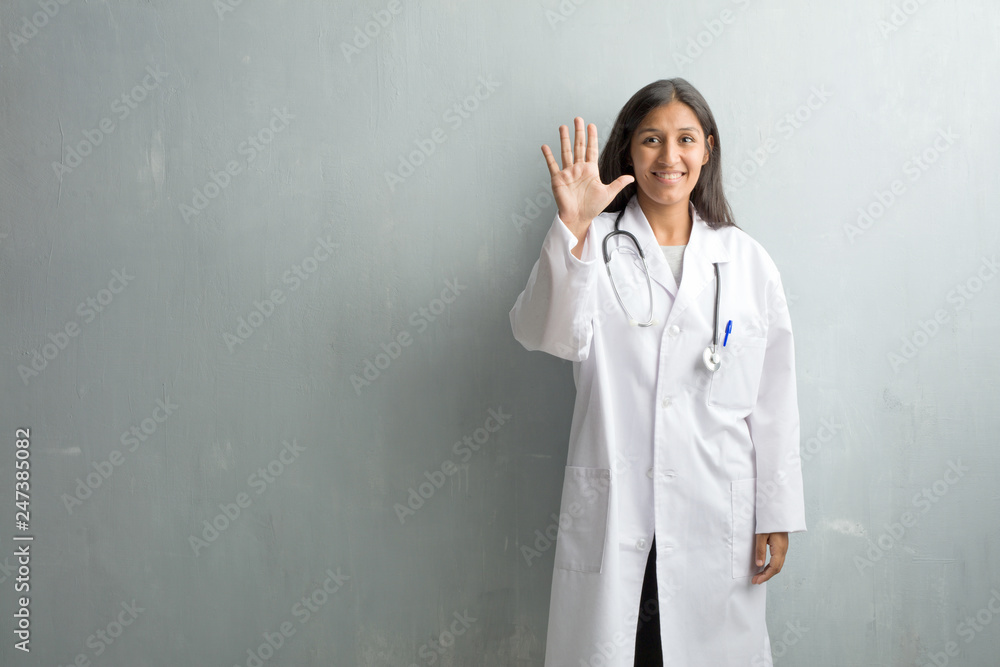 Young indian doctor woman against a wall showing number five, symbol of counting, concept of mathematics, confident and cheerful Young indian doctor woman against a wall showing number five, symbol of counting, concept of mathematics, confident and cheerful