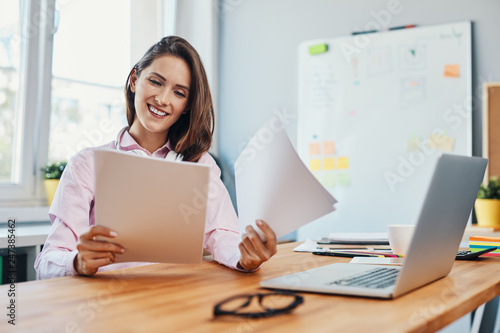 Smiling young woman looking at business documents working in home office photo