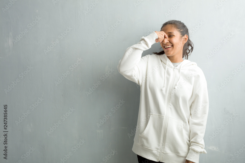 Young sporty indian woman against a gym wall laughing and having fun, being relaxed and cheerful, feels confident and successful
