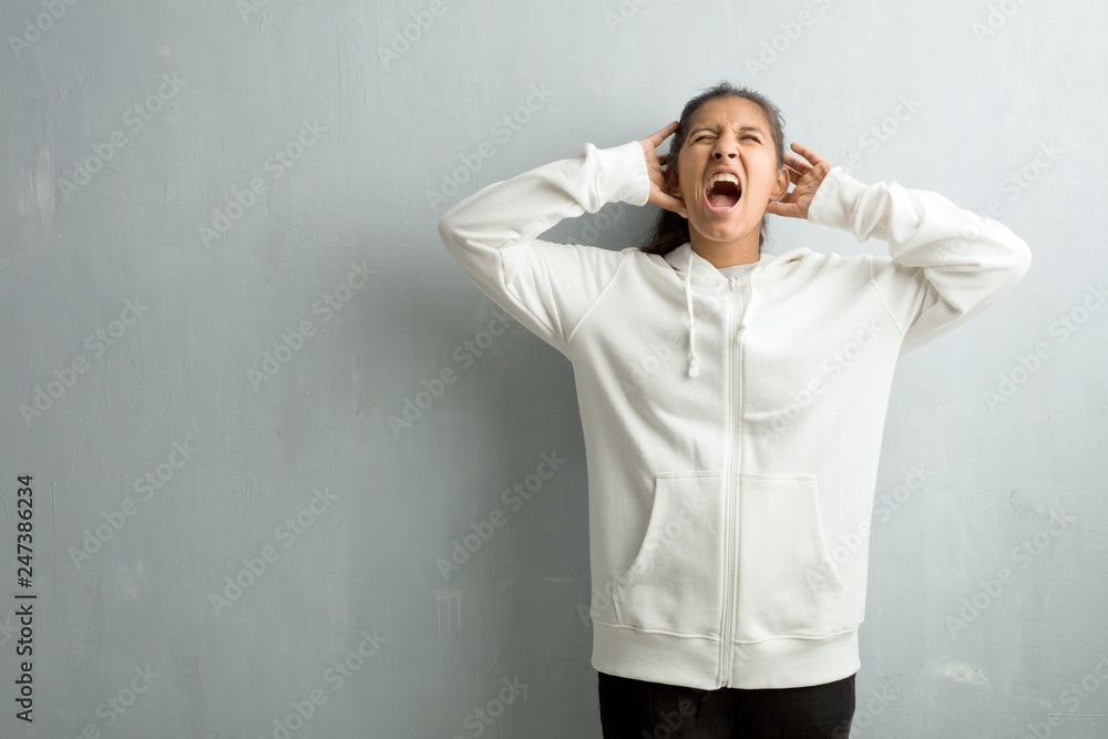 Young sporty indian woman against a gym wall crazy and desperate, screaming out of control, funny lunatic expressing freedom and wild Young sporty indian woman against a gym wall crazy and desperate, screaming out of control, funny lunatic expressing freedom and wild