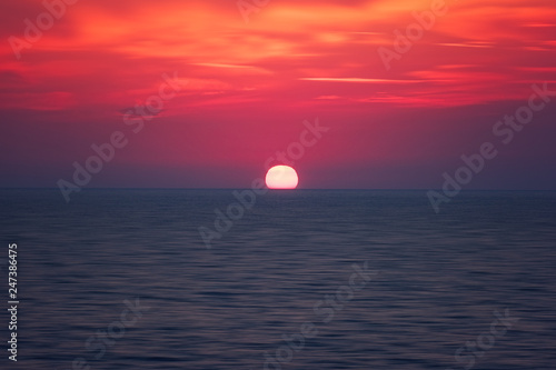 Scenic sunset seascape with sea  sun and amazing scarlet cloudy sky  outdoor travel background  motion blur