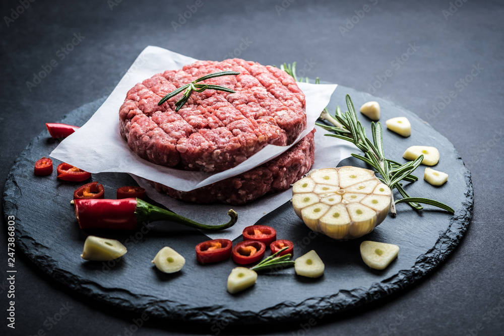 Raw ground beef meat burger steak cutlet with chili, rosemary and garlic on black slate plate for cooking Raw ground beef meat burger steak cutlet with chili, rosemary and garlic on black slate plate for cooking
