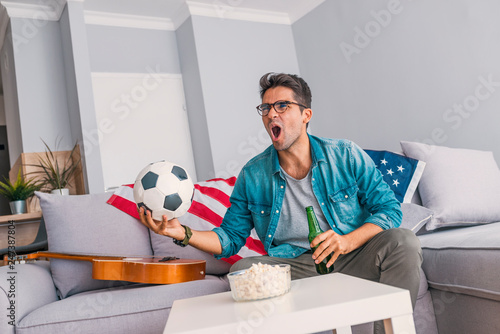 Young man home alone watching soccer or football game in television enjoying and celebrating goal and victory gesturing with fist sitting on the sofa happy and excited © Dragana Gordic