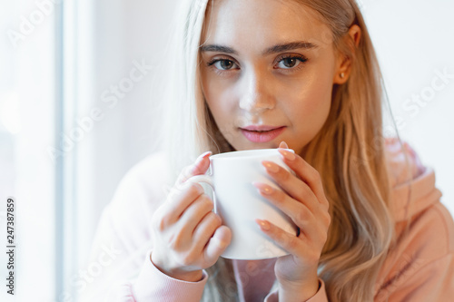 An elf alike  young girl enjoying a cup of coffee or milk while sitting by the window indoors