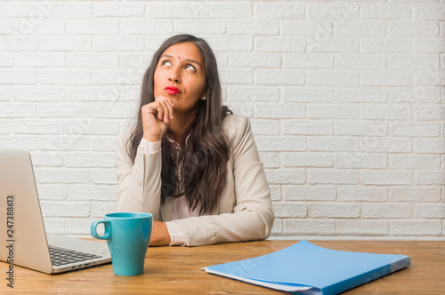 Young indian woman at the office doubting and confused, thinking of an idea or worried about something