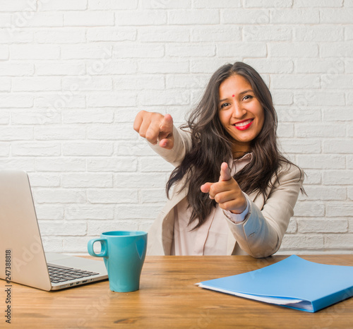 Young indian woman at the office cheerful and smiling pointing to the front