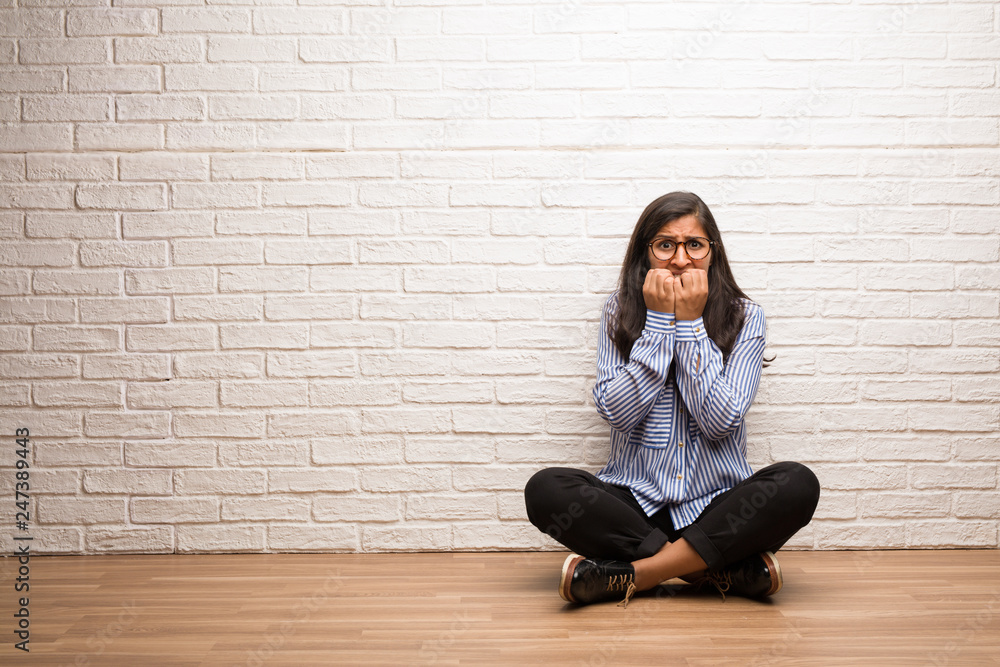 Young indian woman sit against a brick wall biting nails, nervous and very anxious and scared for the future, feels panic and stress Young indian woman sit against a brick wall biting nails, nervous and very anxious and scared for the future, feels panic and stress