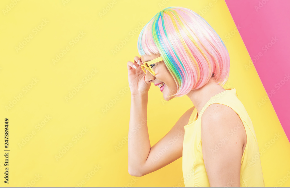 Young woman in a colorful wig with sunglasses on a split yellow and pink background Young woman in a colorful wig with sunglasses on a split yellow and pink background