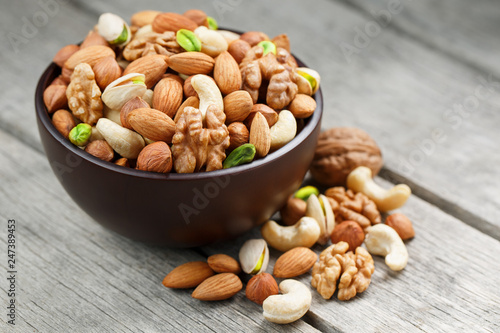 Wooden bowl with mixed nuts on a wooden gray background. Walnut, pistachios, almonds, hazelnuts and cashews, walnut.