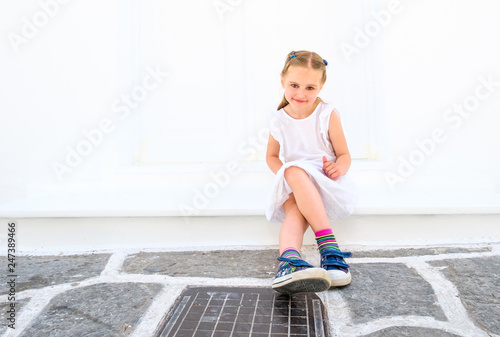 Little pretty blong girl in a white dress sitting outdoor on a street photo