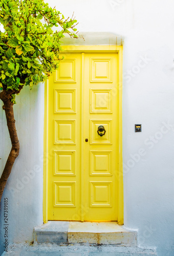 Fototapeta Naklejka Na Ścianę i Meble -  Front view of the white building with yellow door and green tree on greek street