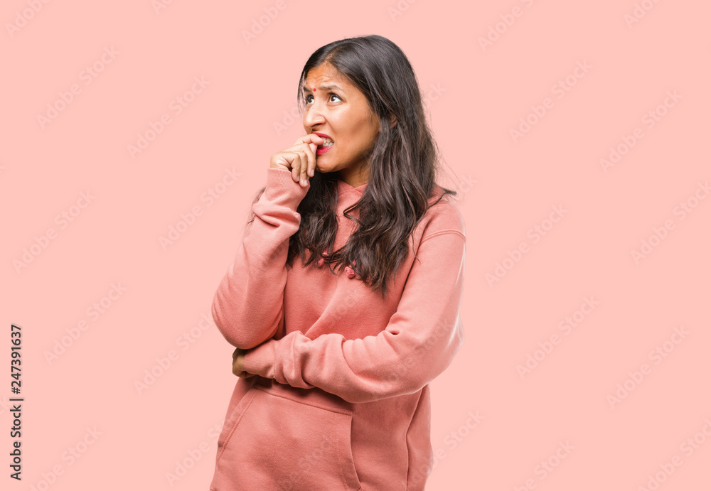 Fototapeta premium Portrait of fitness young indian woman biting nails, nervous and very anxious and scared for the future, feels panic and stress