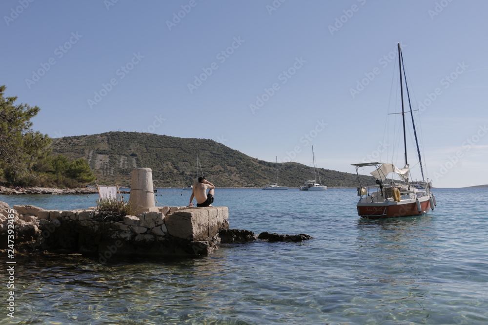 Sailboats, yachts on the Adriatic Sea. Beautiful weather. Sunny, hot, summer day on the Croatian coast. Resting man sunbathing on the rock. Primosten, Croatia. Shore, mediterranean, riviera.