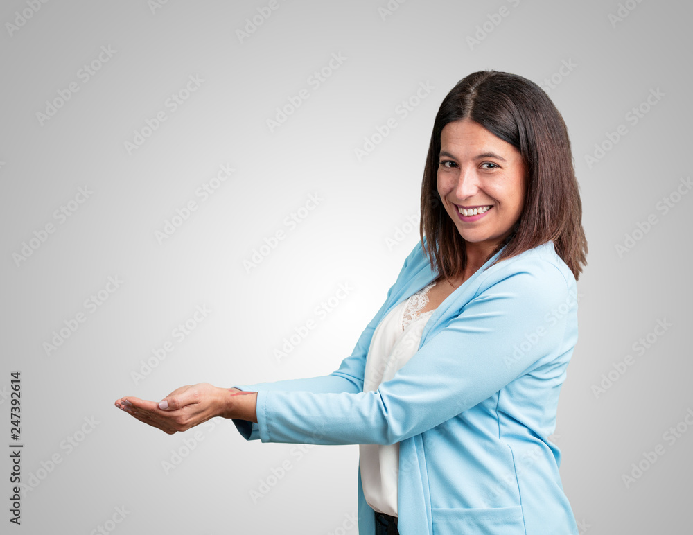 Middle aged woman holding something with hands, showing a product, smiling and cheerful, offering an imaginary object Middle aged woman holding something with hands, showing a product, smiling and cheerful, offering an imaginary object